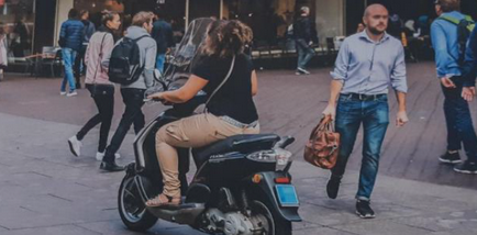 Afbeelding van een vrouw op een scooter die door de straat rijdt.